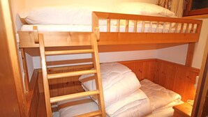Un lit superposé avec une échelle en bois, une literie blanche et une petite table de chevet.