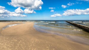 Ein Strand mit einer Holzsteganlage, die sich ins Wasser erstreckt, blauem Himmel und sandigem Ufer.