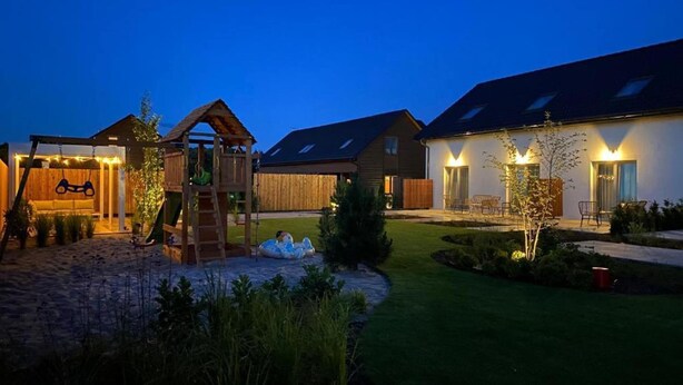 Ein Wohnhaus mit einer Holzspielanlage, einer überdachten Sitzgelegenheit und einer gut beleuchteten Terrasse mit Gartenmöbeln.