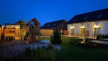 A residential property with a wooden play structure, a covered seating area, and a well-lit patio with outdoor furniture.