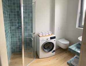 Bathroom features a clear shower enclosure, washing machine, and a grid-patterned tile design.