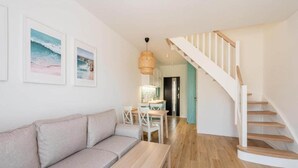 Ein modernes Wohnzimmer mit einem beigefarbenen Sofa, einem Holztisch und einer Treppe, die zu einer weiteren Ebene führt.