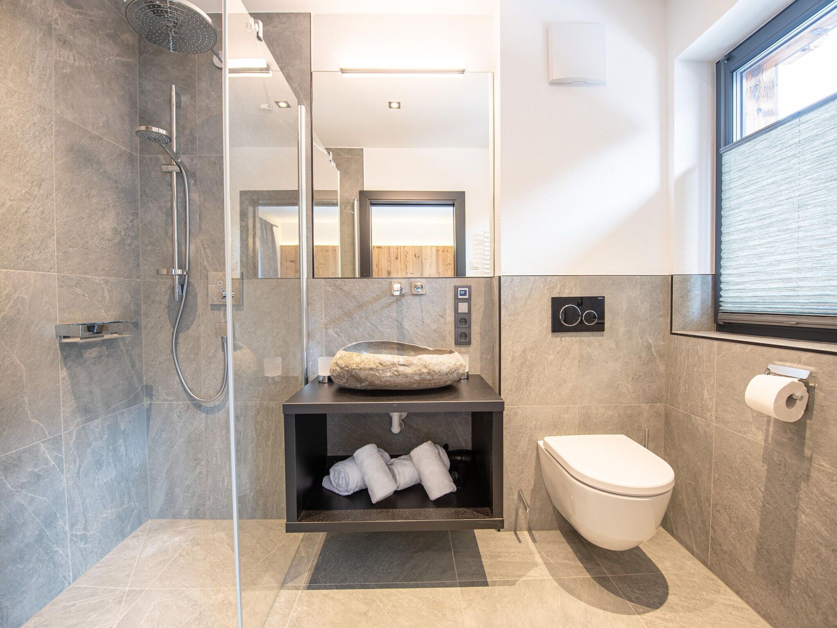 A modern bathroom with a glass-enclosed shower, a built-in sink with a stone basin, a toilet, and a mirror.