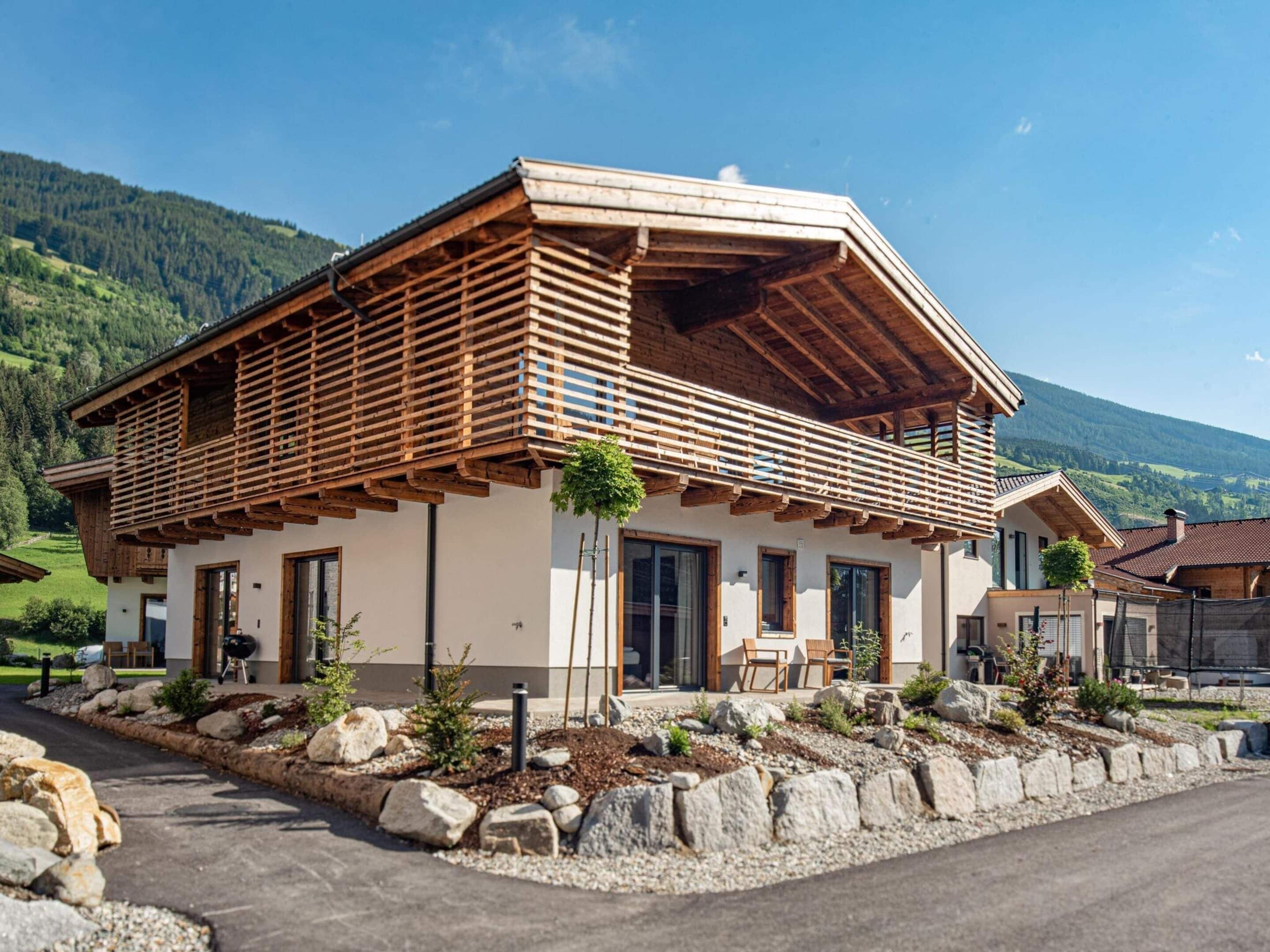 Een modern chalet met een schuin dak, houten balkon en een pad van stenen dat naar de ingang leidt.