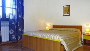 Un letto singolo con struttura in legno e copripiumino a righe, due lampade sui comodini, un quadro appeso alla parete e una finestra con tende blu.
