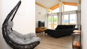 A living room with a hanging chair, a black sofa, a wooden coffee table, and a TV. - Ferienwohnung mit Sauna (Inzell)