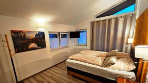 A bedroom with a bed, a desk, a lamp, a painting, and a window with curtains. - Ferienwohnung mit Sauna (Inzell)