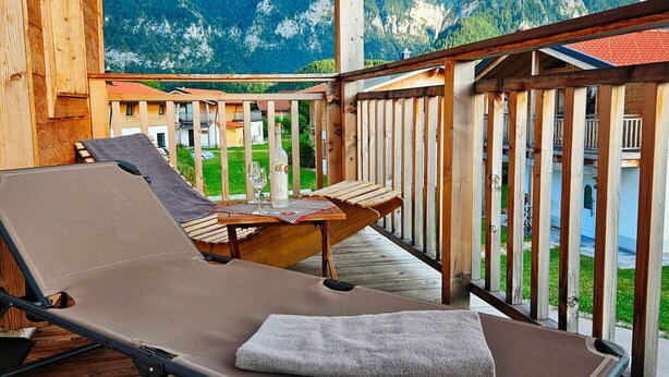 A wooden deck with a lounge chair and a table, overlooking a mountainous landscape. - Ferienwohnung mit Sauna (Inzell)