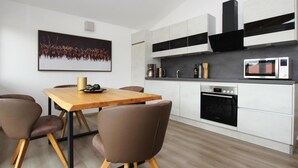 A modern kitchen with white cabinets, a microwave, and a coffee maker. There is a wooden dining table with chairs and a framed picture on the wall. - Ferienwohnung mit Sauna (Inzell)