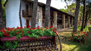 A rustic building with a stone facade, wooden balconies, and a garden with red flowers. - Grado Apartment in Belvedere Resort (Aquileia)