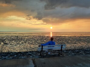 Eine Person sitzt auf einer Bank und blickt auf einen Sonnenuntergang über dem Wasser.