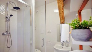 Un baño moderno con cabina de ducha de vidrio, un inodoro blanco, un lavabo con espejo y un estante de madera con una planta.