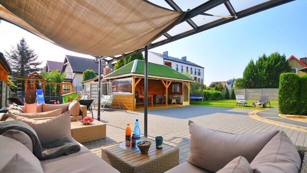 Un patio al aire libre con una zona de estar cubierta, una estructura de juego de madera y una barbacoa.