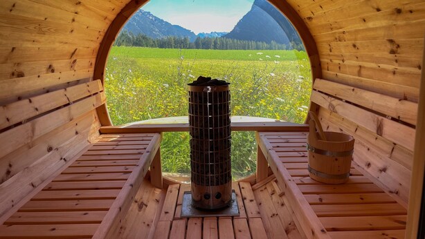 Une cabane en bois dotée d’une fenêtre circulaire qui offre une vue sur un champ verdoyant et des montagnes.
