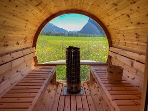 Une cabane en bois dotée d’une fenêtre circulaire qui offre une vue sur un champ verdoyant et des montagnes.