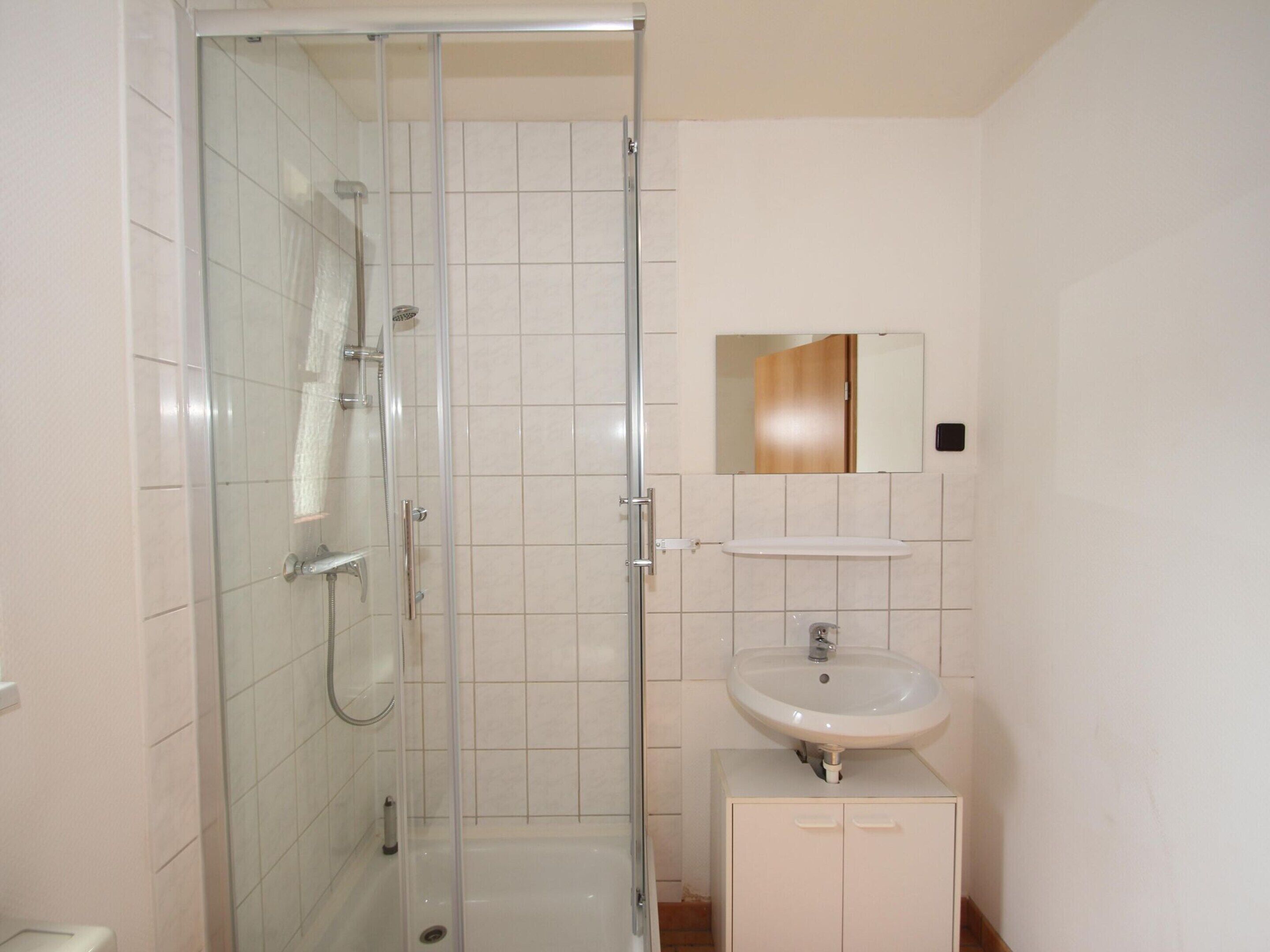 A bathroom with a glass-enclosed shower, a white sink, and a mirror above the sink.