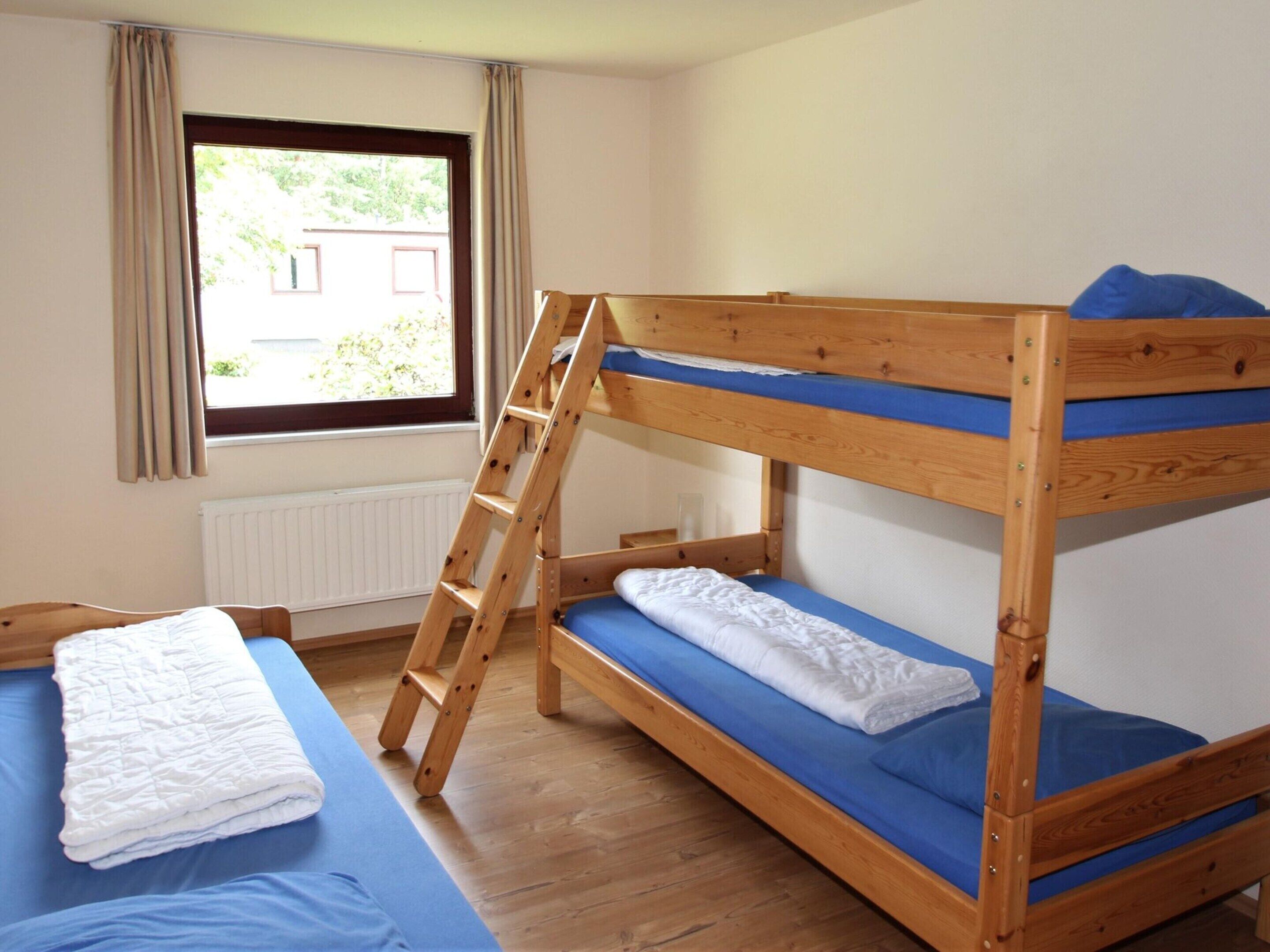A bunk bed with a wooden ladder, a single bed with a blue mattress, and a window with curtains.