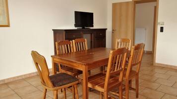 A dining room with a wooden table and chairs, a television on a cabinet, and a door leading to another room.