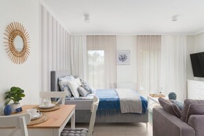 Et moderne, godt oplyst værelse med en seng, en sofa, et spisebord med stole og et fjernsyn på væggen.