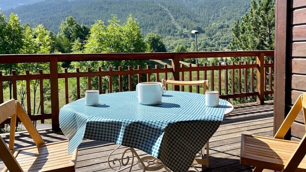 Une terrasse en bois avec une table dressée pour deux personnes, offrant une vue sur un paysage montagneux.