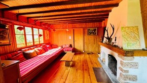 L’intérieur d’un chalet accueillant, avec un plancher en bois, un canapé, une cheminée et une fenêtre donnant sur un paysage agréable.