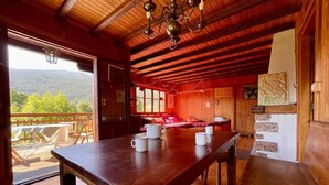Un intérieur en bois avec une grande table, des sièges rembourrés de couleur rouge et une vue sur un paysage montagneux, visible à travers une grande fenêtre.