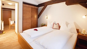 Een tweepersoonsbed met witte lakens, een houten hoofdbord en een houten plafondbalk.