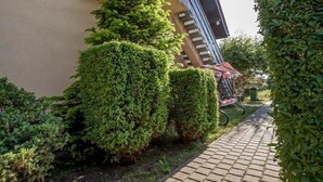 Un chemin pavé longe un bâtiment, avec des haies soigneusement taillées et un vélo garé à proximité.
