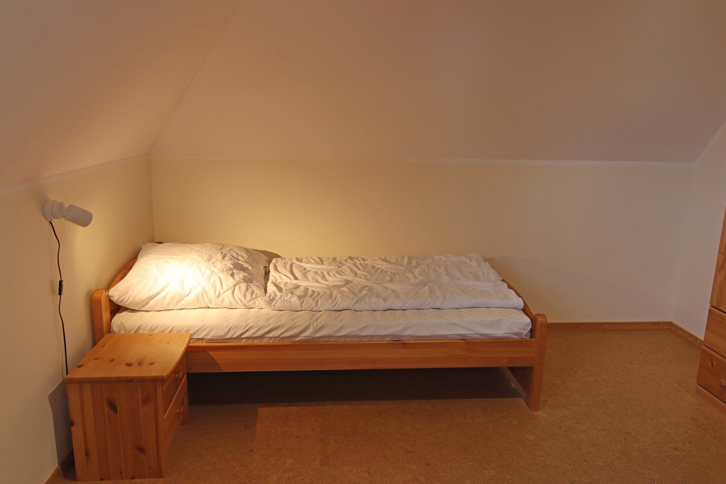 Una habitación pequeña con una cama individual, un cabecero de madera, una mesita de noche y una lámpara de pared.