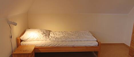 Una habitación pequeña con una cama individual, un cabecero de madera, una mesita de noche y una lámpara de pared.