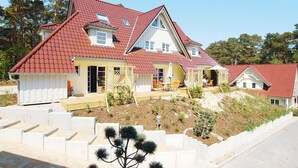 A two-story house with a red-tiled roof, a front porch with outdoor seating, and a landscaped garden. - Reihenhaus Dunenwaldhaus in Trassenheide (Trassenheide)