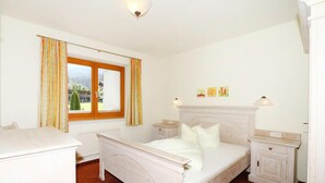 Ein Schlafzimmer mit Bett, Nachttischen, einem Schminktisch und einem Fenster mit Vorhängen.