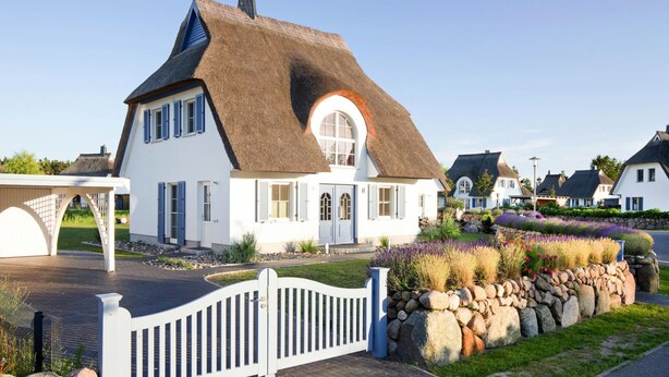 Une maison blanche avec un toit de chaume et une clôture en bois peinte en blanc.