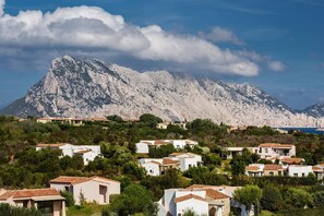 A coastal village with white buildings and terracotta roofs, surrounded by greenery and a mountain in the background. - Appartement Grande Baia Resort, San Teodoro (San Teodoro)