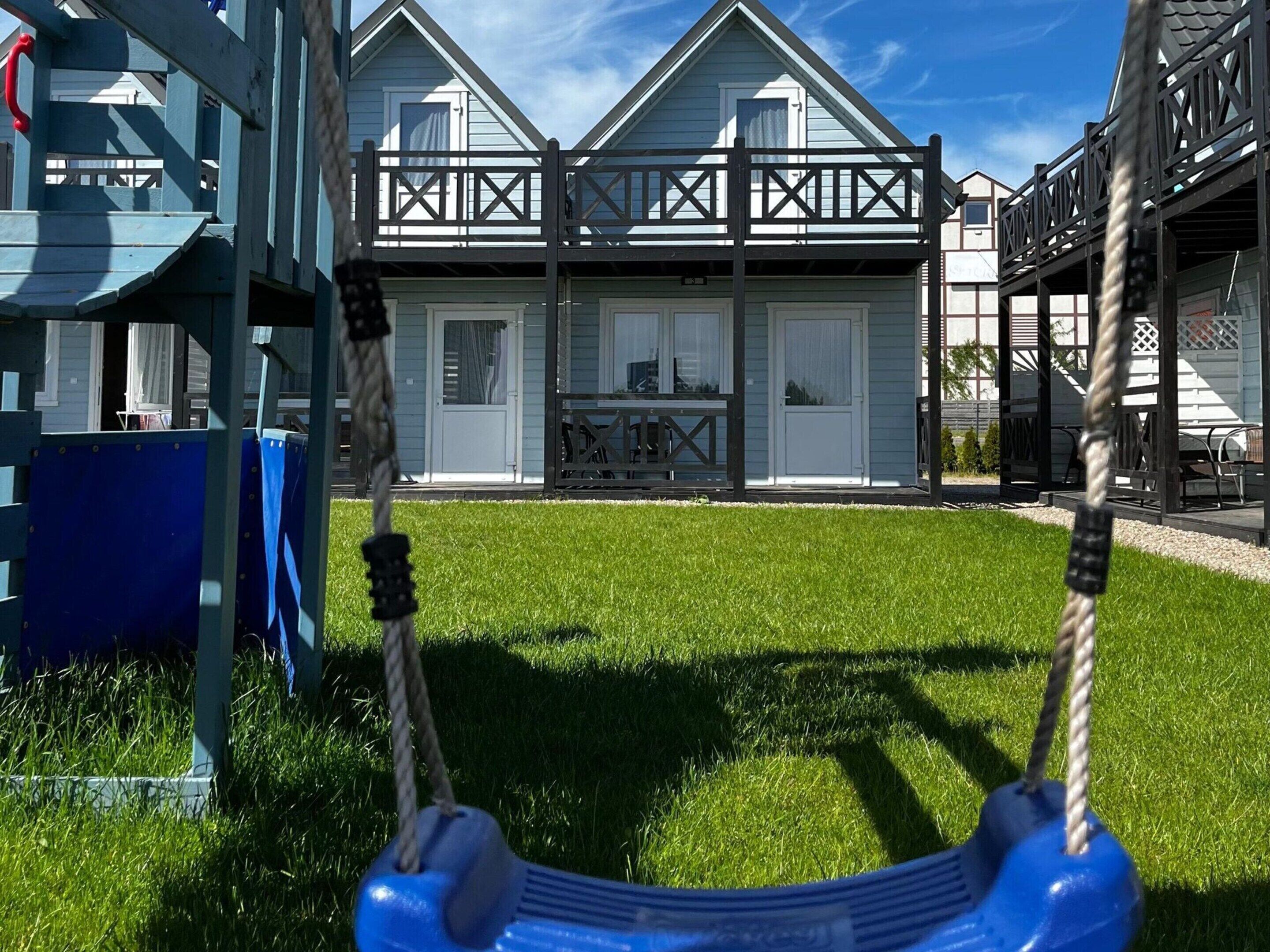 A playground with a swing set and a building with a balcony in the background.