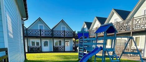 A residential area with a grassy yard, a blue slide, and a wooden deck.