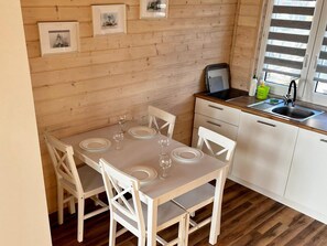 A compact kitchen with a dining area, wooden walls, and a window with blinds. - Holiday Home Pobierowo Near Beach & Pool (Rewal)
