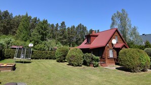 Une cabane en bois avec un toit rouge, entourée de pelouses et d’arbres bien entretenus.