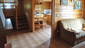 L’intérieur d’une cabane comprend un coin repas, une cuisine et un espace de vie confortable avec un canapé et une cheminée.