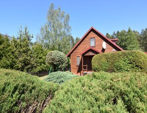 A wooden cabin with a red roof, surrounded by dense greenery and tall trees.