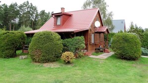 Une maison en bois avec un toit rouge, entourée d’arbustes bien entretenus et d’une cour gazonnée.