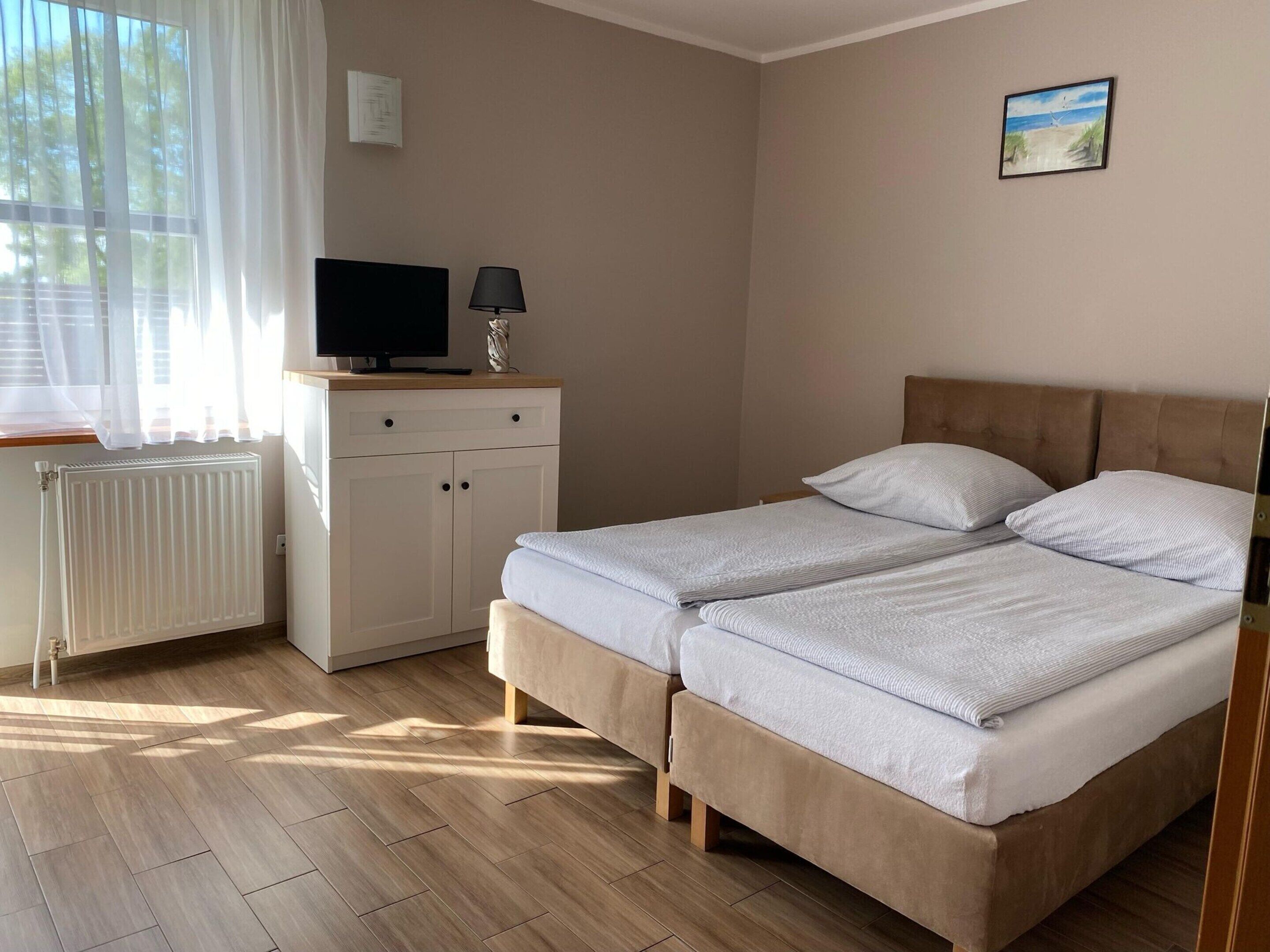 Une chambre avec deux lits, un bureau avec une télévision, un radiateur et une fenêtre avec des rideaux.