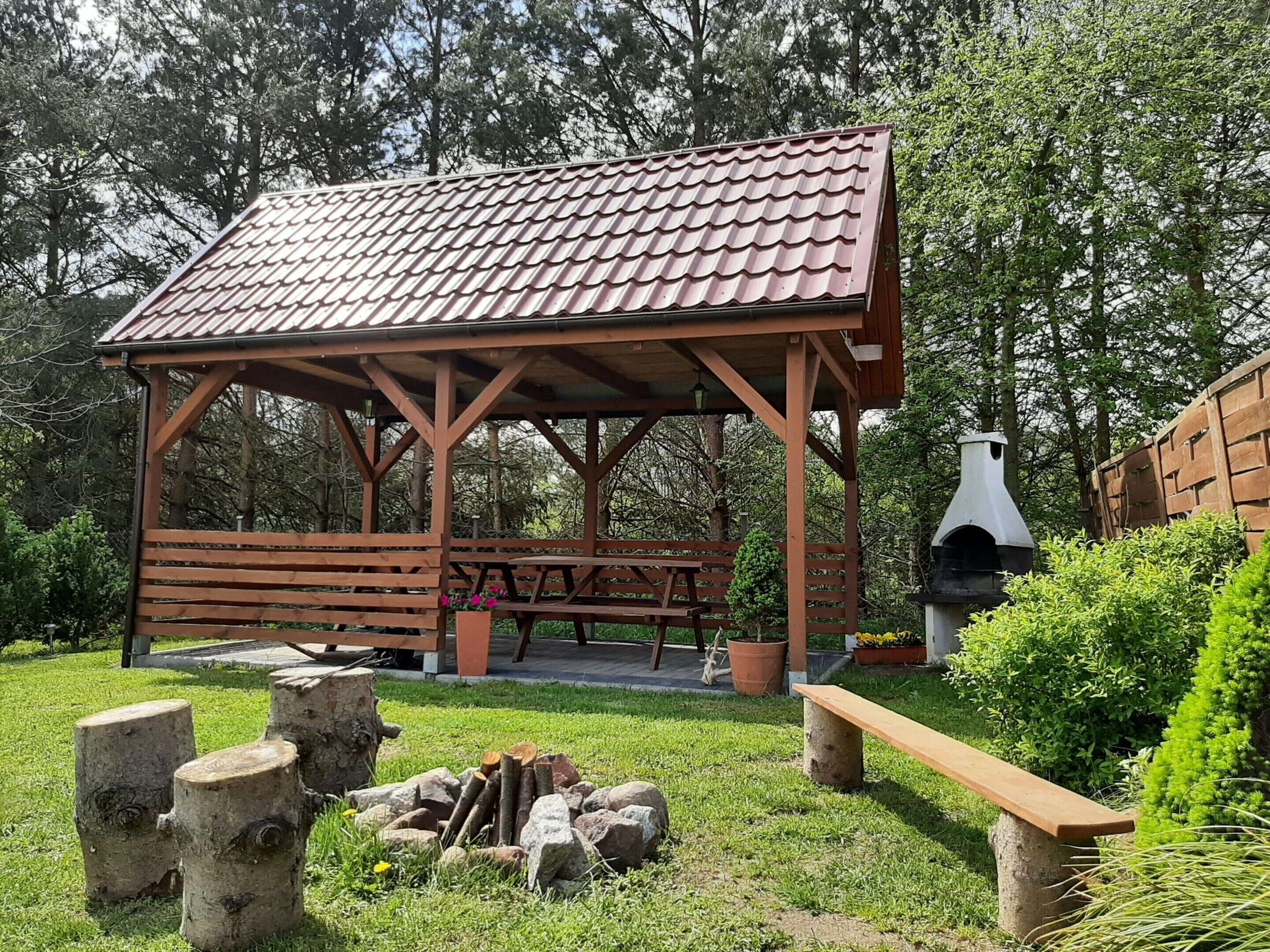 A wooden pavilion with a tiled roof, a picnic table, and a wood-fired oven.