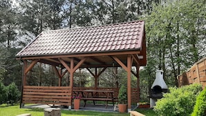 Un padiglione in legno con tetto in tegole, un tavolo da picnic e un forno a legna.