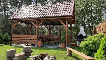 A wooden pavilion with a tiled roof, a picnic table, and a wood-fired oven.