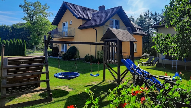 Una casa con un balcone, un'altalena e uno scivolo nel giardino.