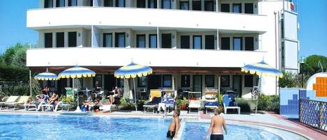 A hotel with a pool area, multiple balconies, and outdoor seating with umbrellas.