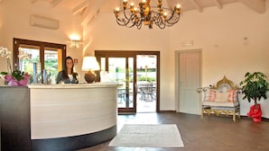 A reception area with a curved counter, a chandelier, and a bench with a plant. - Holiday Residence Punta Falcone Near Beach (Santa Teresa di Gallura)