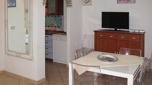A compact kitchen with a dishwasher, a dining table with chairs, a TV on a wooden cabinet, and a decorative mirror. - Apartment on Costa Rei Near Sandy Beaches (Muravera)