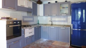 A kitchen with grey cabinets, a blue refrigerator, and a tiled backsplash. - Apartment on Costa Rei Near Sandy Beaches (Muravera)